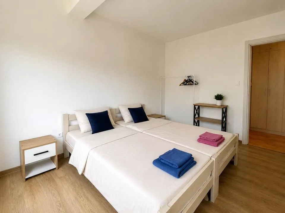 Svijetla spavaća soba sa dva spojena kreveta i noćnim stočićima.