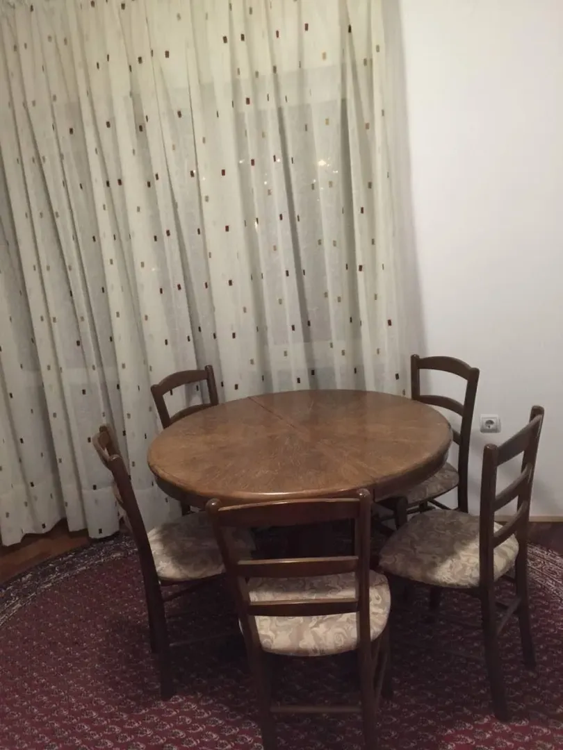 Drveni trpezarijski sto sa četiri stolice pored prozora.