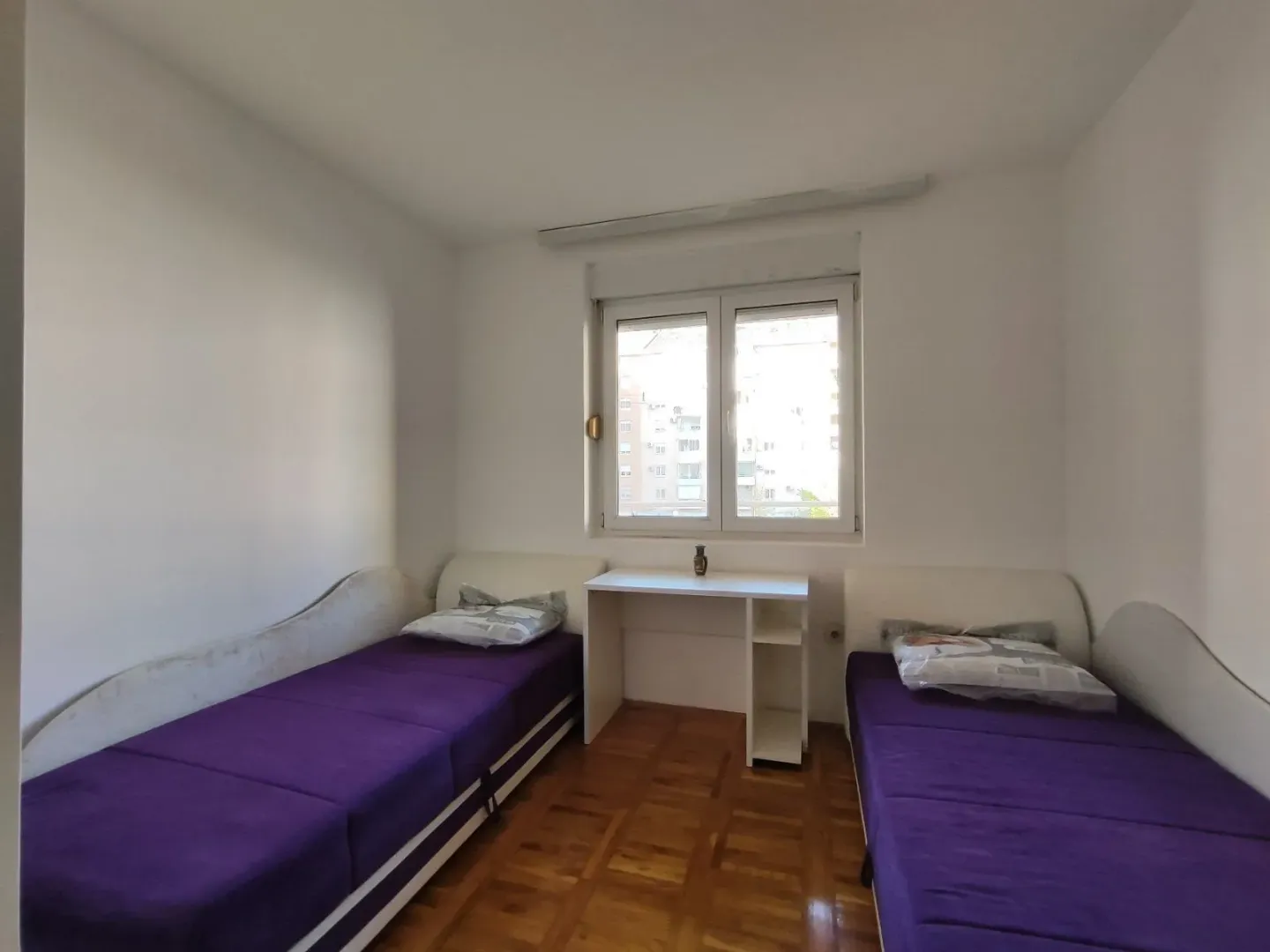 Svijetla spavaća soba sa dva kreveta i radnim stolom.