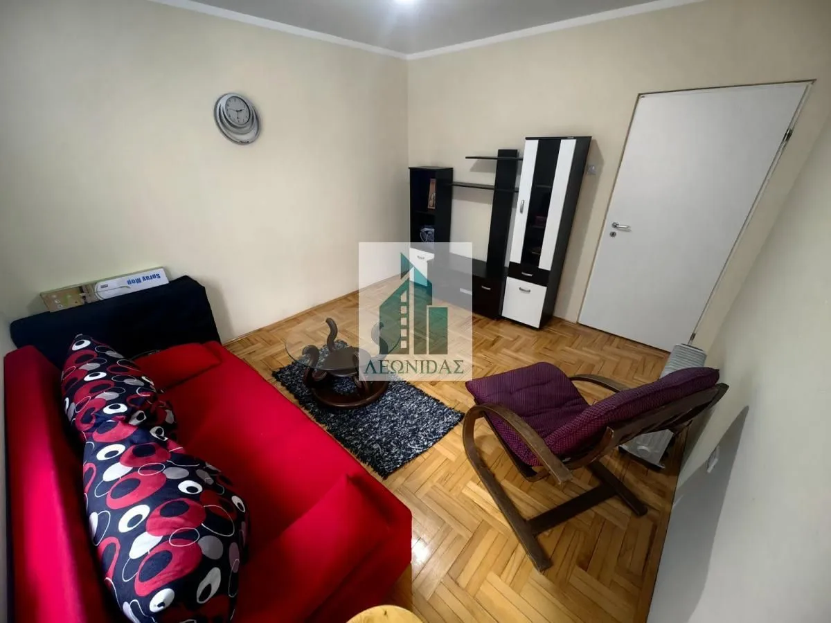 Smaller living room with a red sofa, armchair, and parquet flooring.