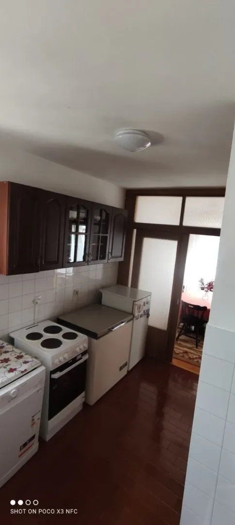 Kuhinja sa tamnim drvenim visećim elementima i električnim šporetom.