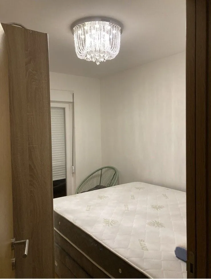 View from the hallway into a bedroom with a bed and a chandelier.