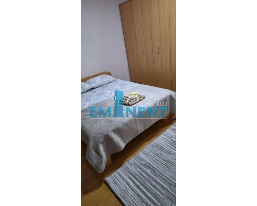 Nameštena spavaća soba sa bračnim krevetom i drvenim ormarom.