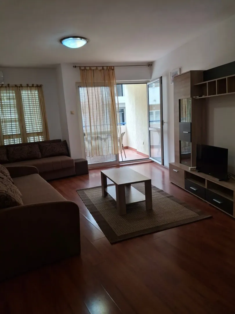 Dnevna soba sa garniturom, TV komodom i izlazom na terasu.