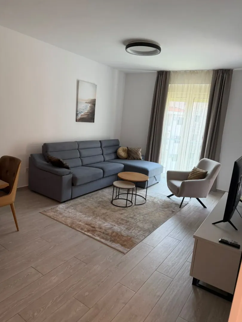 Svijetao dnevni boravak sa ugaonom garniturom, foteljom i trpezarijskim stolom.