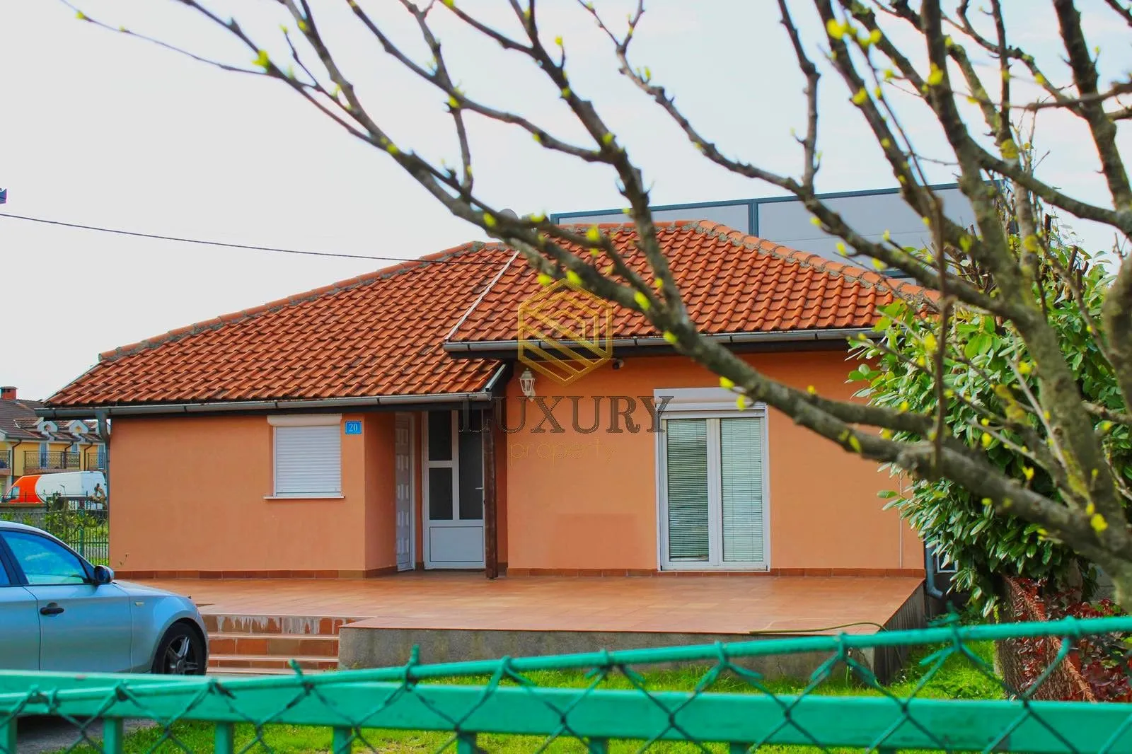 Pogled na prednju fasadu kuće sa popločanim dvorištem i krovom od crijepa.