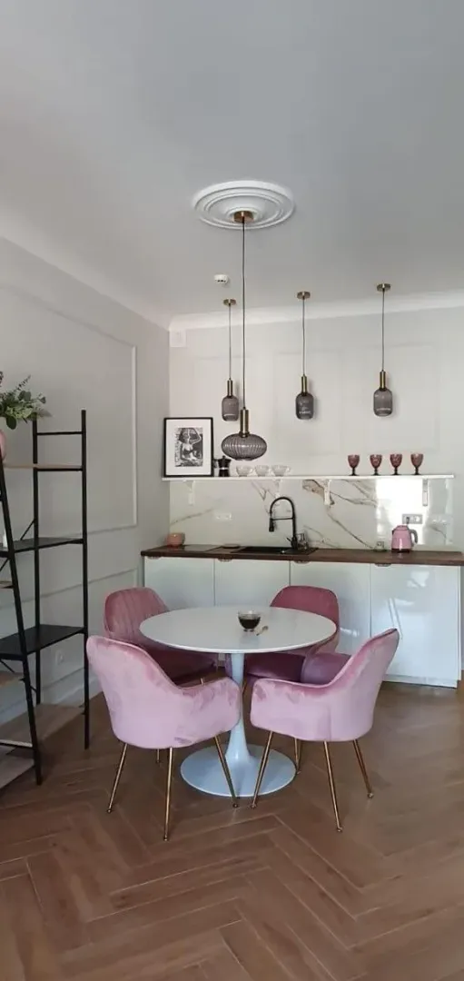 Trpezarija sa modernim stolom i roze stolicama uz ugradnu kuhinju.