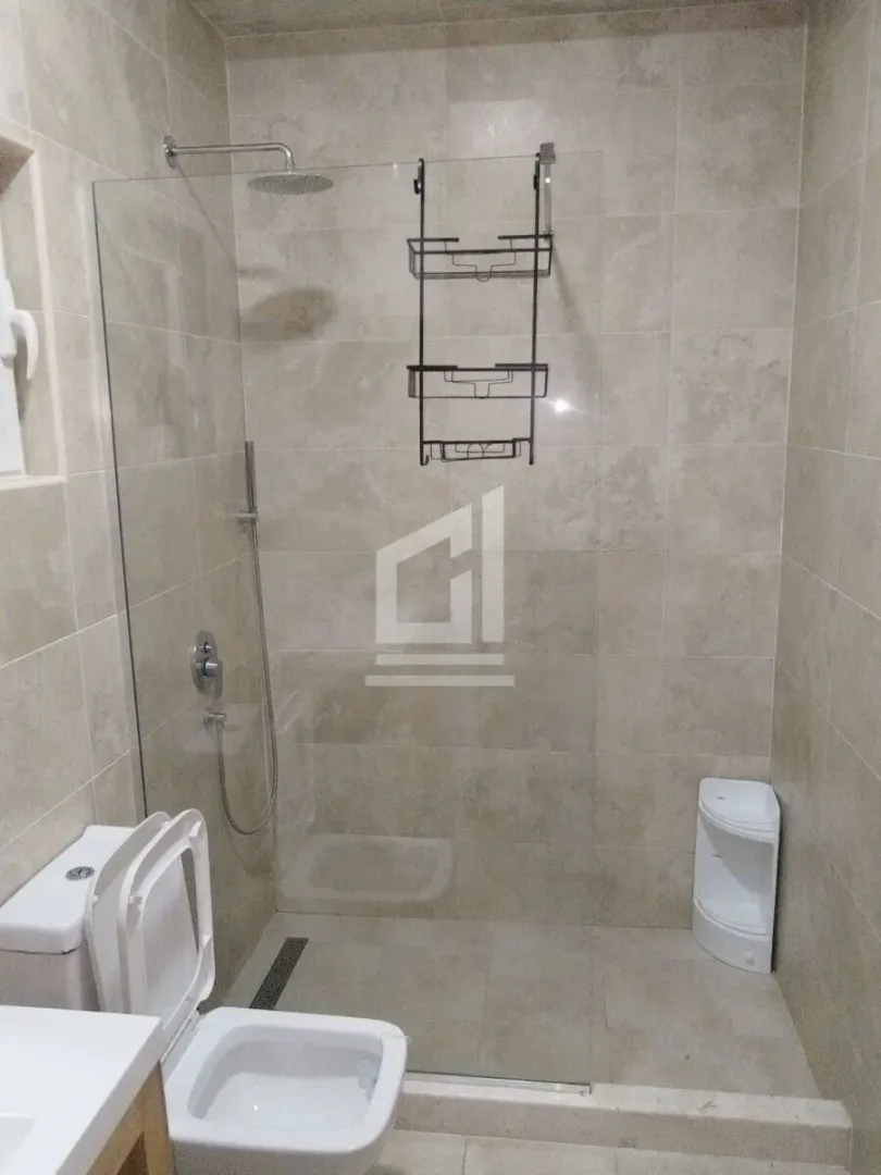 Kupatilo sa tuš kabinom i ugradnim sanitarijama obloženo pločicama.