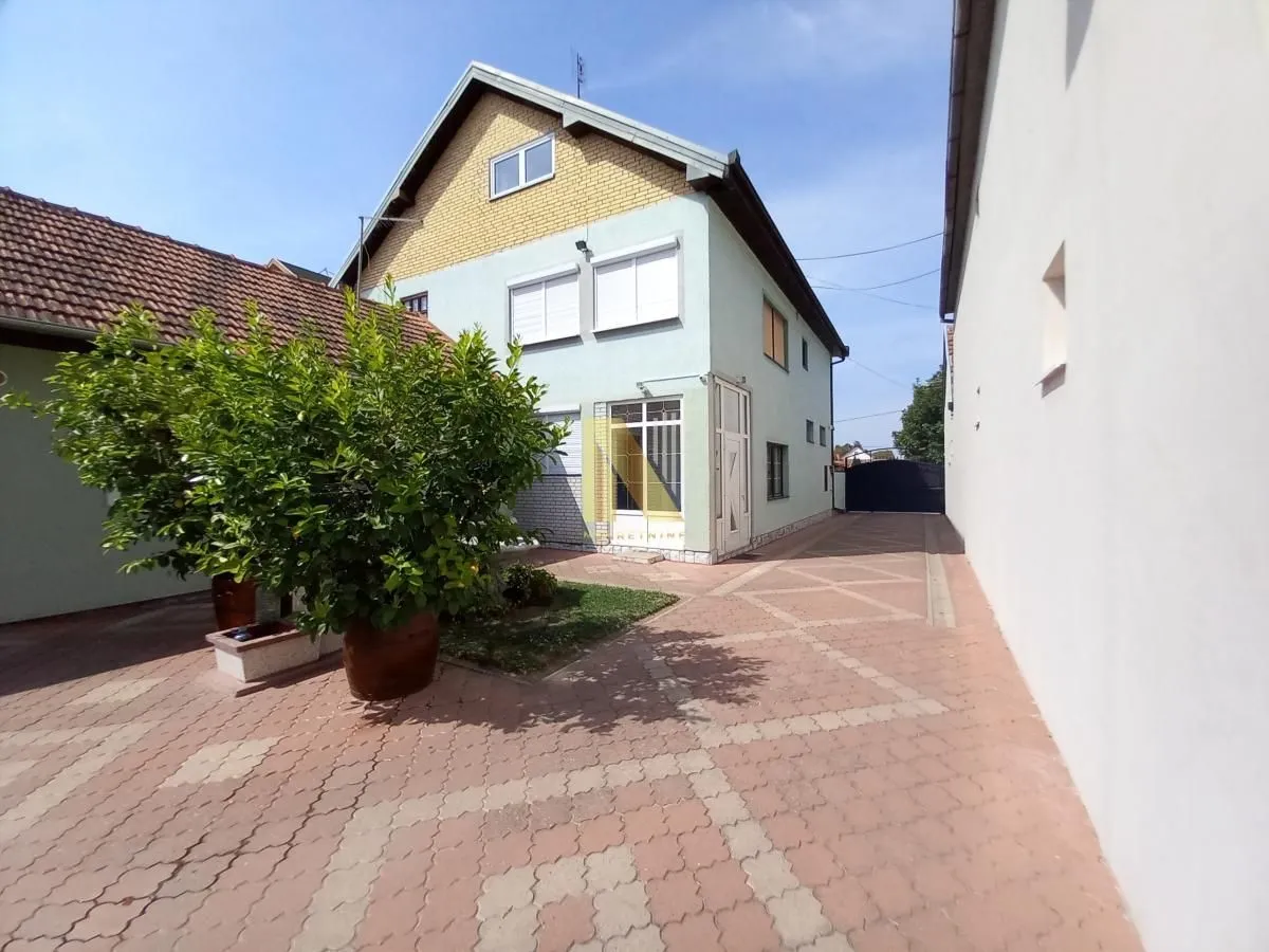 Dvorište porodične kuće sa popločanim prolazom i zelenilom.