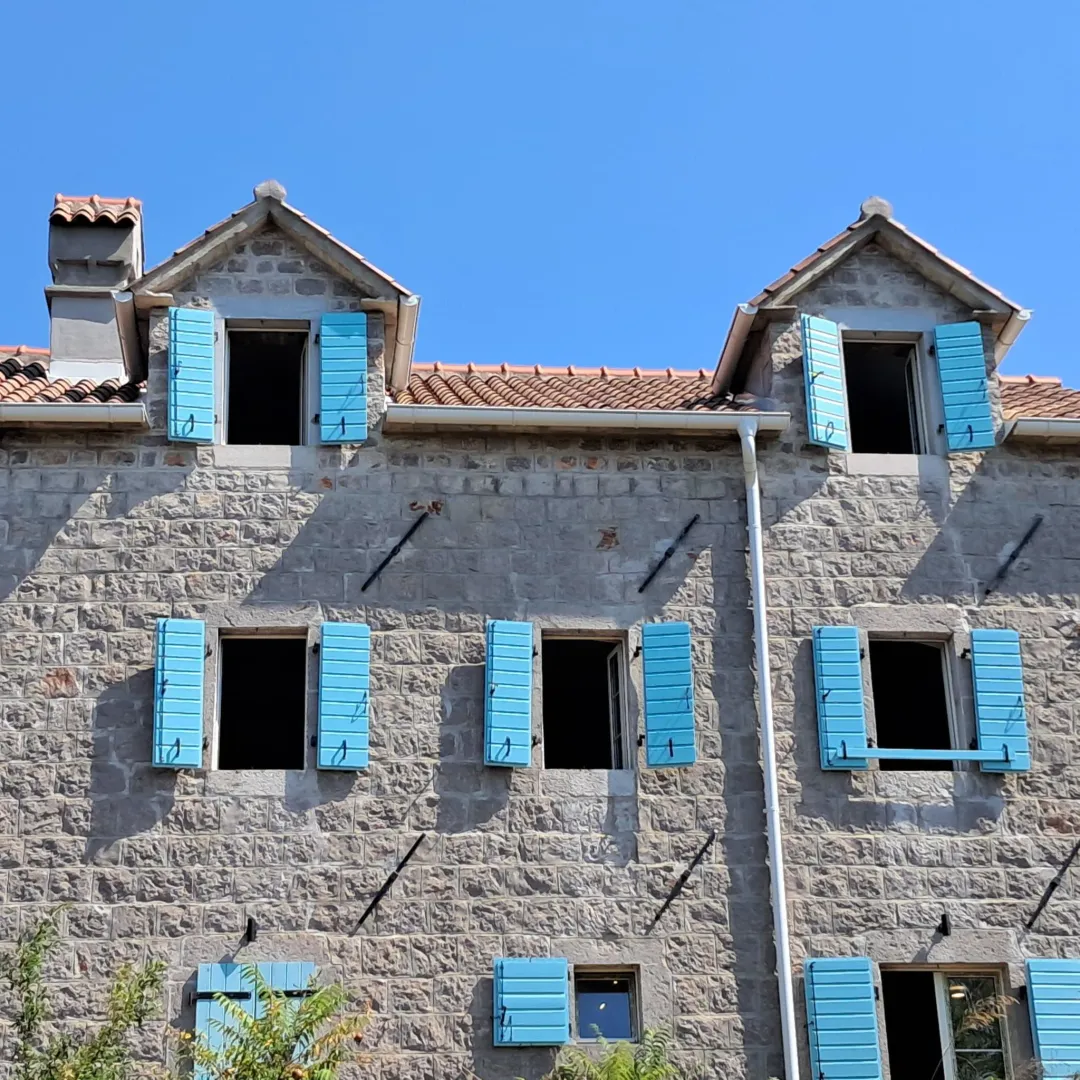 Kamena fasada tradicionalne kuće sa plavim škurama.