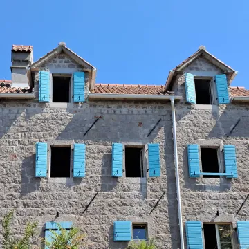 Kamena fasada tradicionalne kuće sa plavim škurama. - image 2