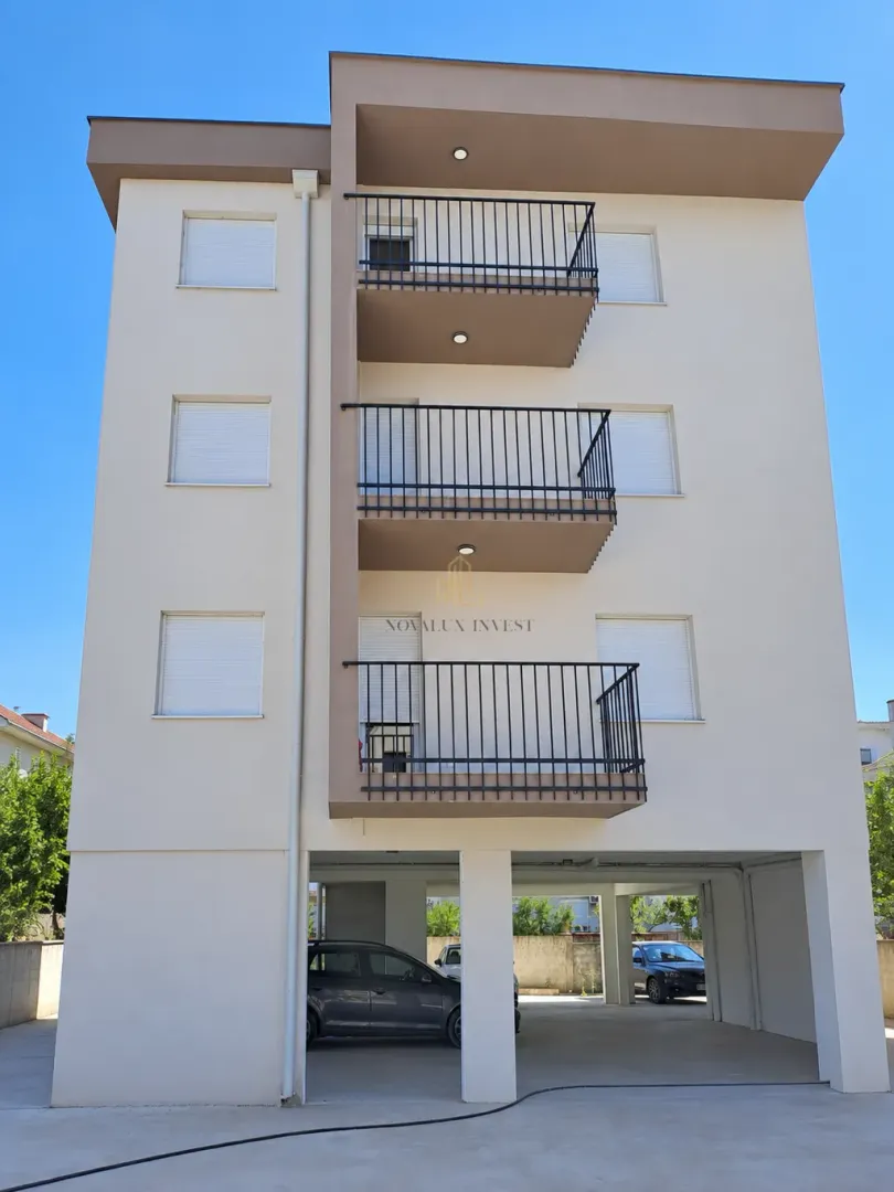 Front facade of an apartment building with balconies and ground floor covered parking.