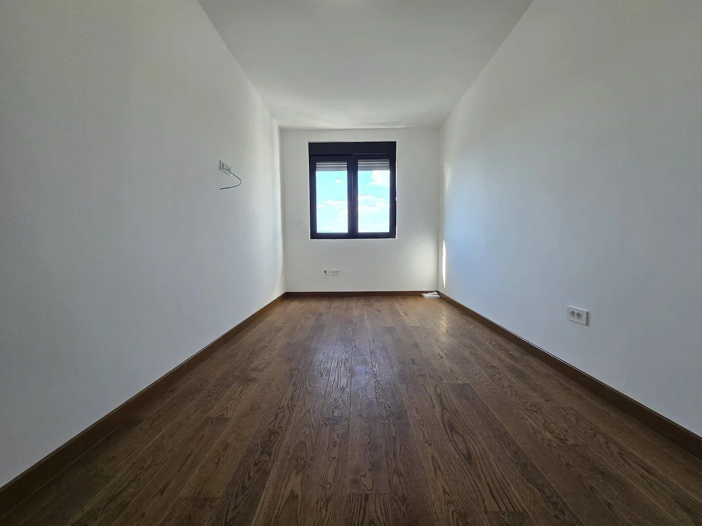 Empty room with white walls, wooden flooring, and a window.