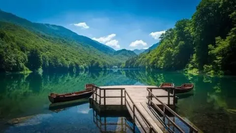 Pogled na jeZERO i drveni mol sa čamcima okružen šumom i planinama. - image 4