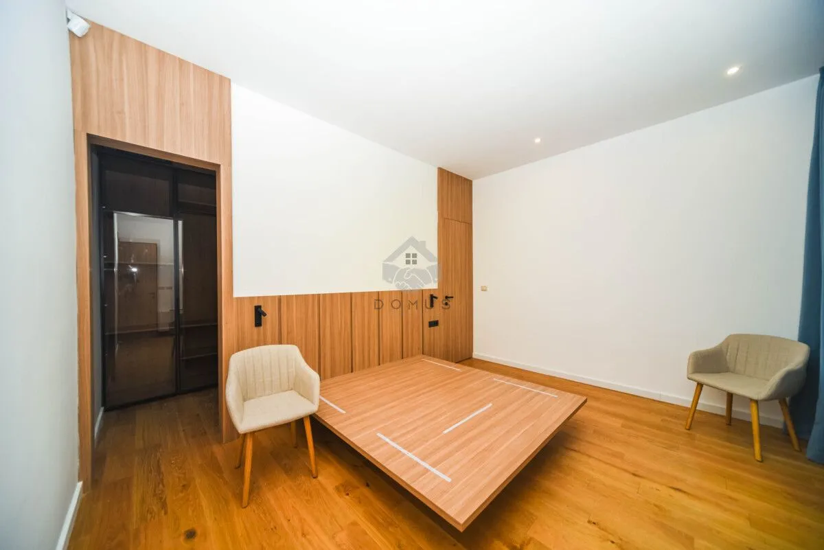Bedroom with wooden bed, flooring and wall paneling, and two armchairs.