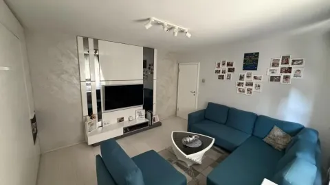 Dnevna soba sa plavom ugaonom garniturom i TV uređajem na zidu. - image 7