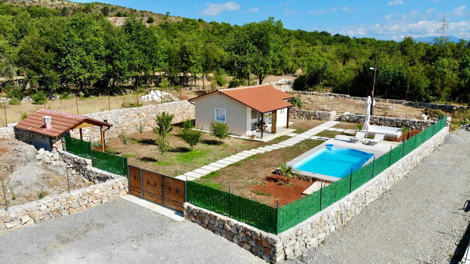 Aerial view of a house with a swimming pool, yard, and stone fence.