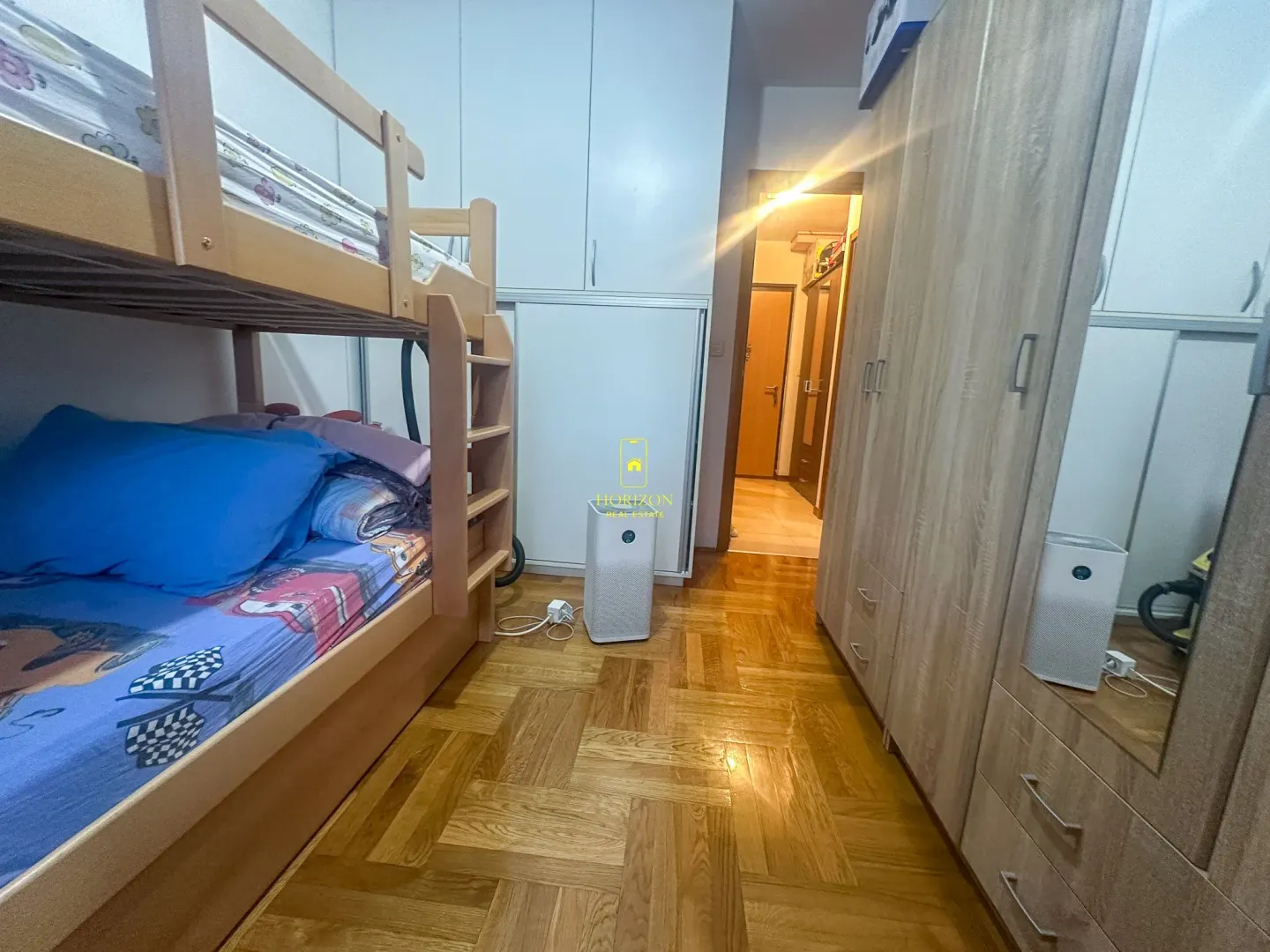 Dječija soba sa krevetom na sprat i drvenim ormarima.