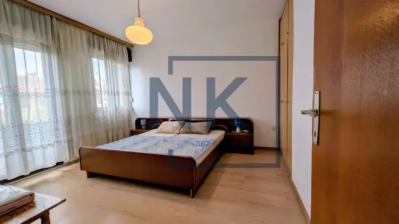 Spacious bedroom with a double bed, wardrobe, and a large window with curtains.