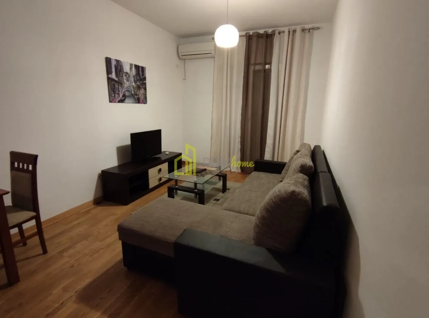 Dnevna soba sa ugaonom garniturom, televizorom i trpezarijskim stolom.
