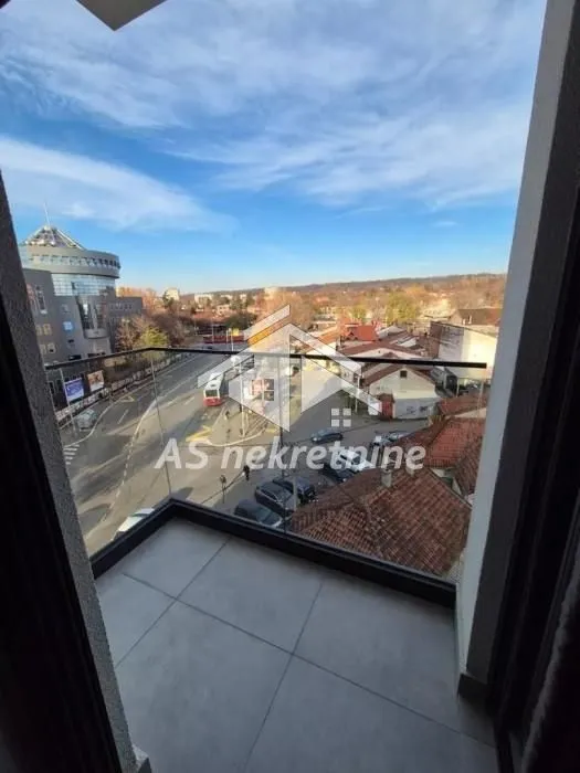 Small tiled balcony with a glass railing and a view of the street and surrounding buildings.