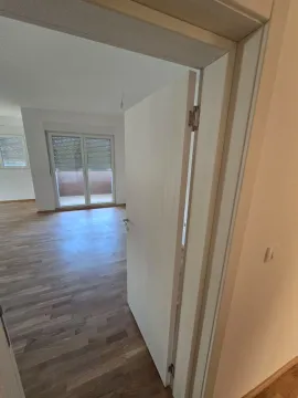 Pogled na svijetao prazan prostor sa drvenim podom kroz otvoren prolaz. - image 4