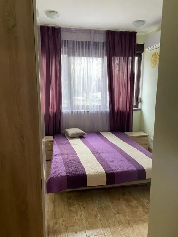 Bedroom with a double bed, a window with purple curtains, and bedside tables.