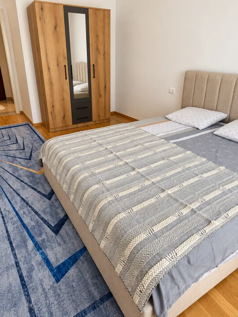 Bedroom with a double bed, wooden wardrobe, and a blue rug.