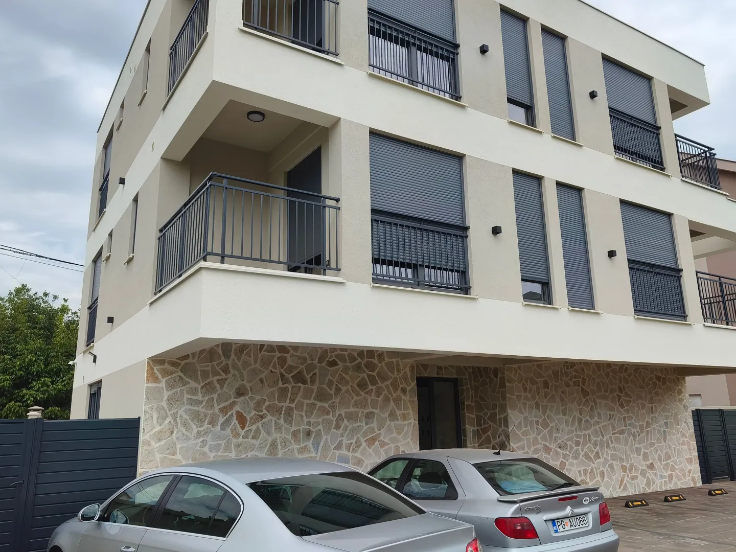 Spoljašnji izgled moderne stambene zgrade sa balkonima i parkingom u prizemlju.