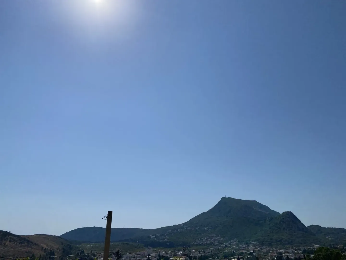 Širok pogled na brda i naselje pod jasnim plavim nebom.