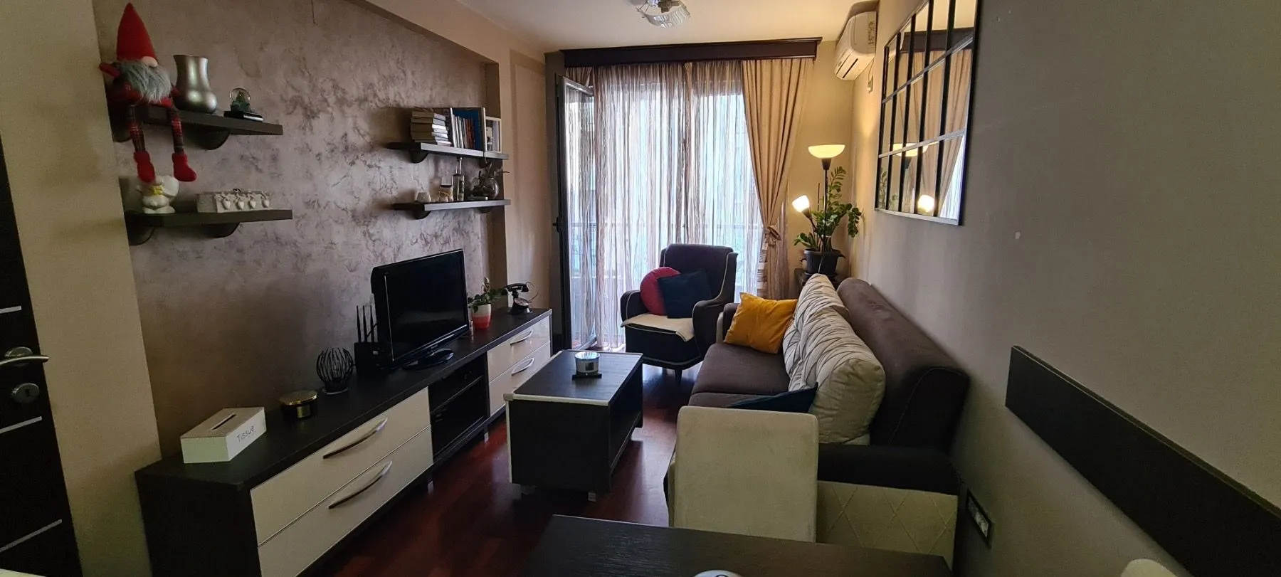 Namještena dnevna soba sa garniturom, TV komodom i izlazom na terasu.