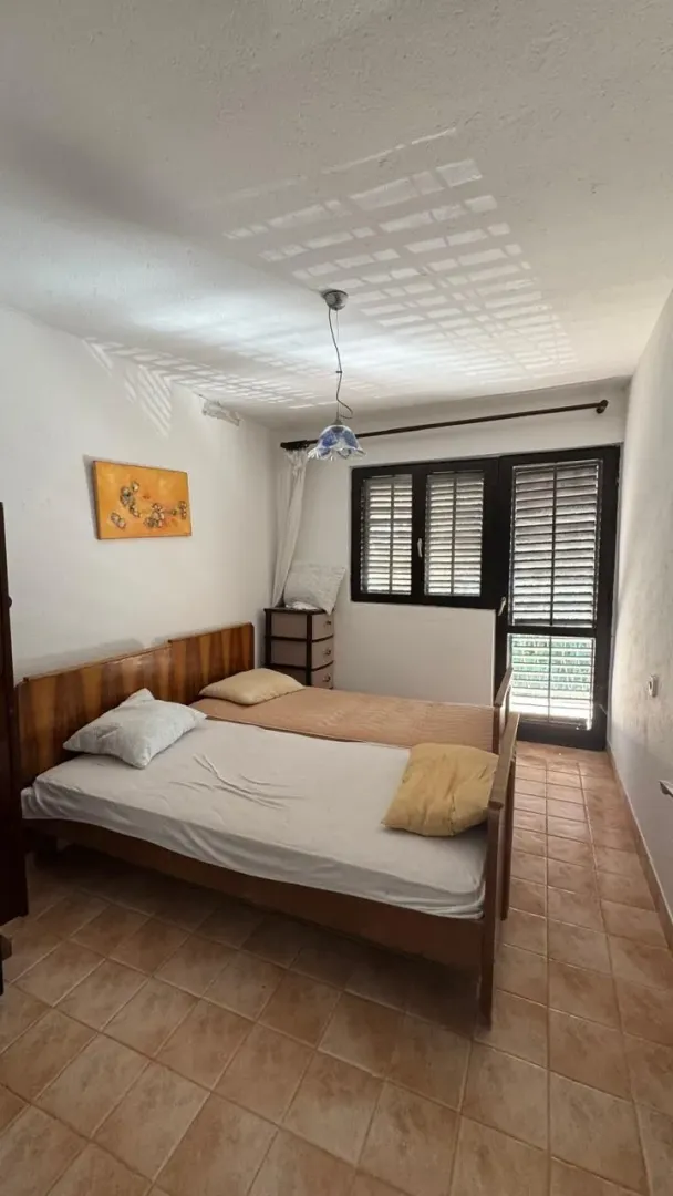 Spavaća soba sa dva drvena kreveta i izlazom na terasu.