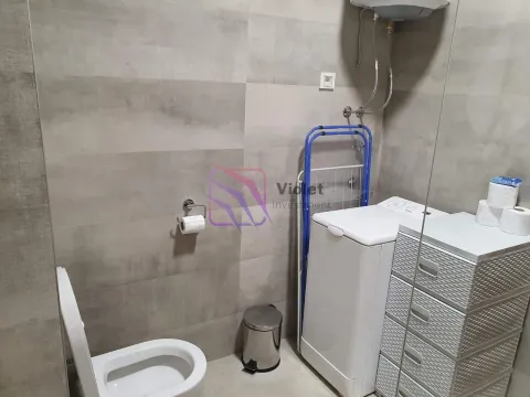Bathroom with a toilet, washing machine, and grey tiles. - image 8