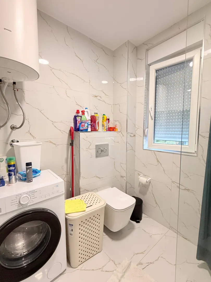 Manje uredno kupatilo sa veš mašinom, WC šoljom i prozorom.