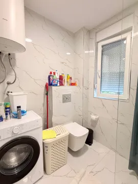 Manje uredno kupatilo sa veš mašinom, WC šoljom i prozorom. - image 7
