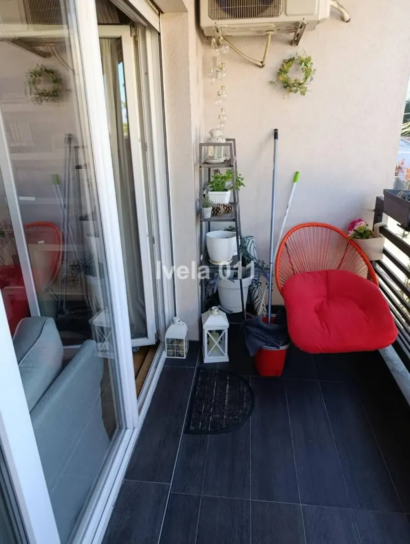 Manji namešteni balkon sa staklenim kliznim vratima i crvenom foteljom.
