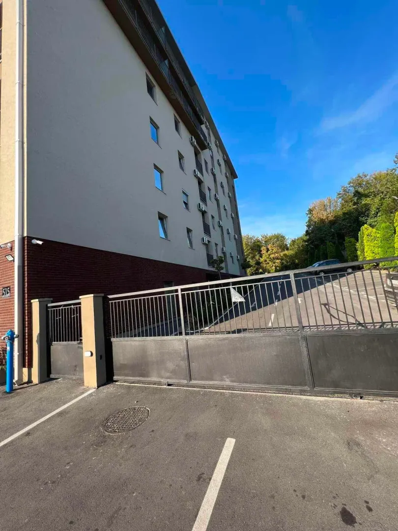 Exterior view of an apartment building with an entrance gate and parking.