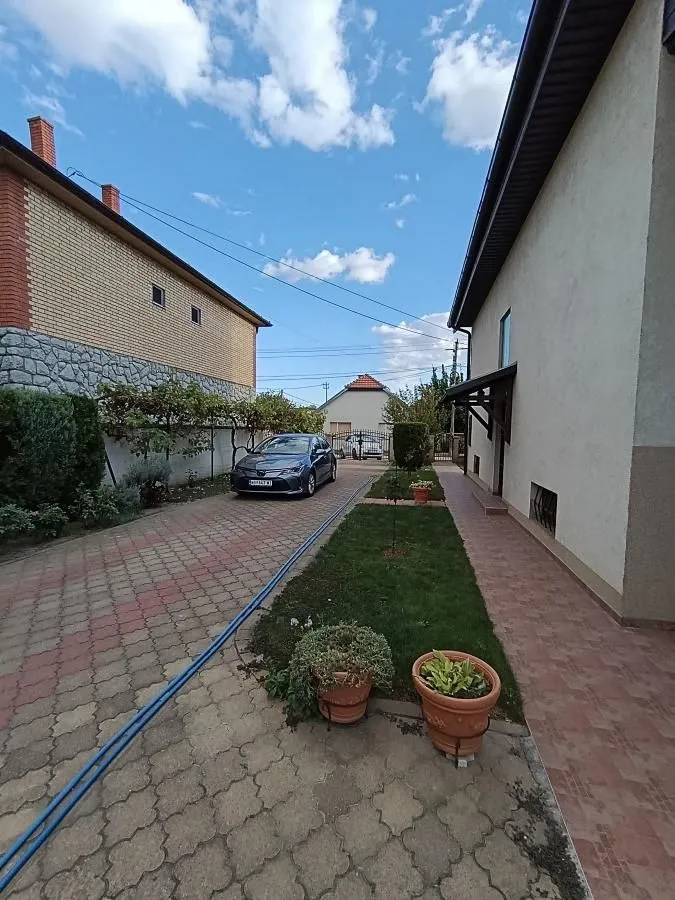 Dvorište sa popločanim stazama i parkiranim automobilom pored kuće.