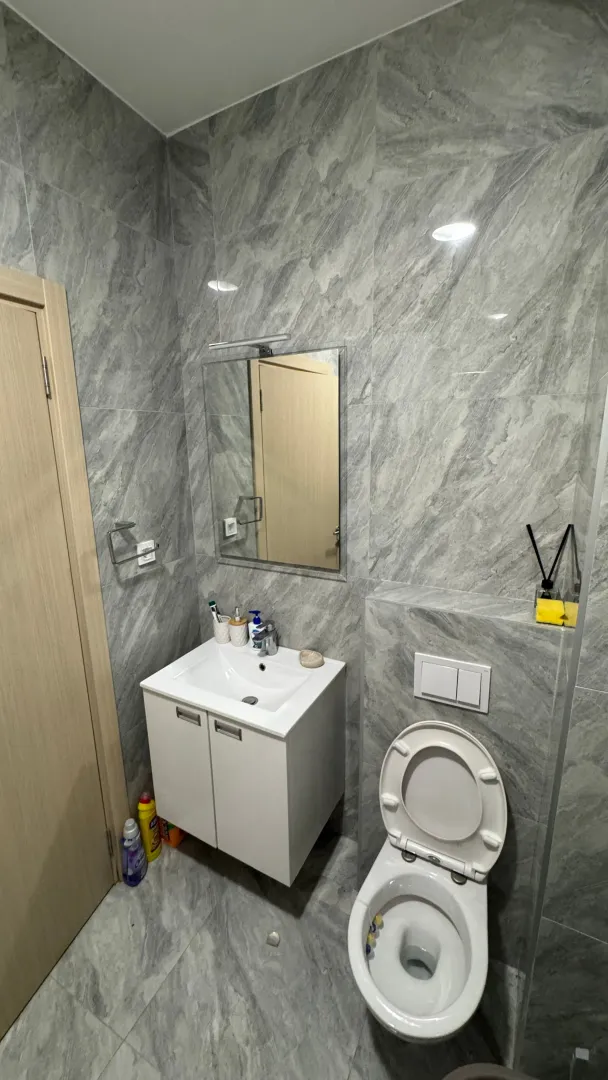 Moderne kupatilo obloženo sivim pločicama sa umivaonikom i wc šoljom.