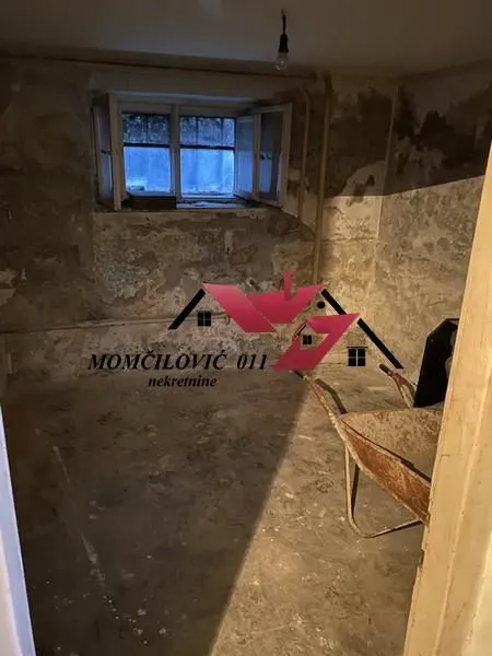 Prazna prostorija u sirovom stanju sa građevinskim kolicima i malim prozorom.