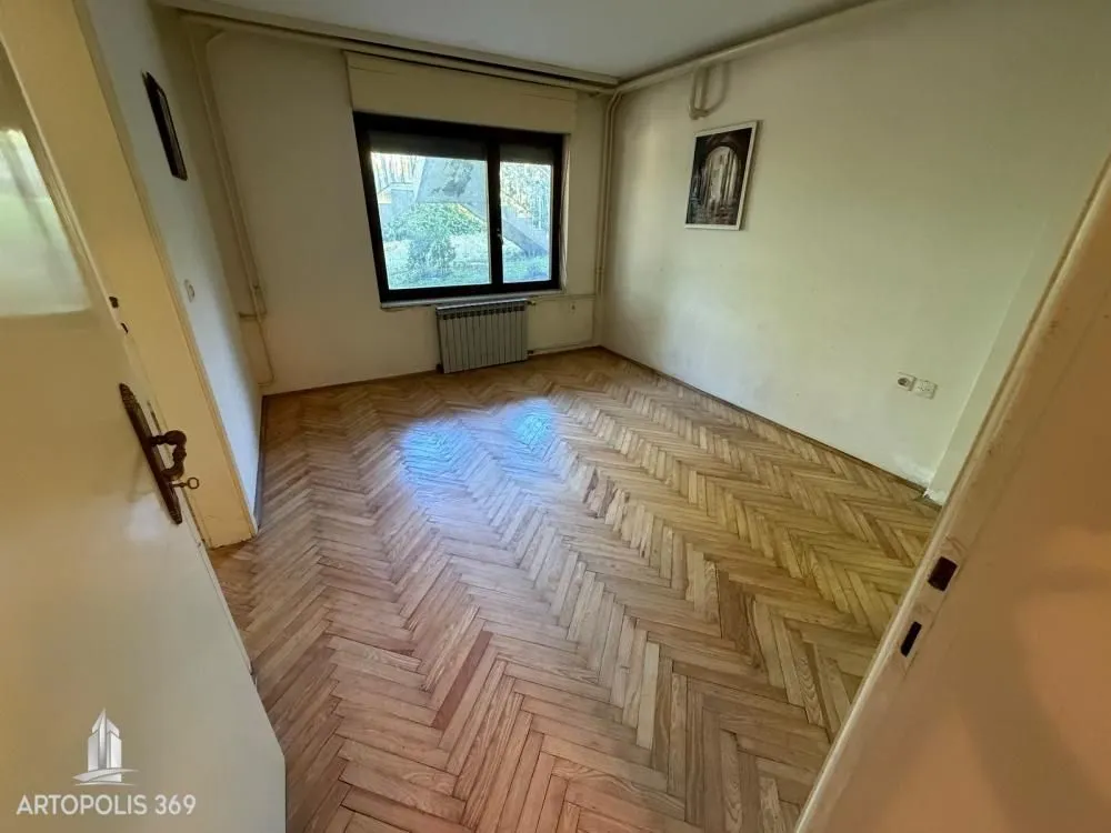 Prazna soba sa drvenim parketom i prozorom.