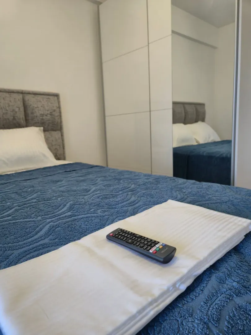 A view of the bed with a blue bedspread and a mirrored wardrobe in the bedroom.