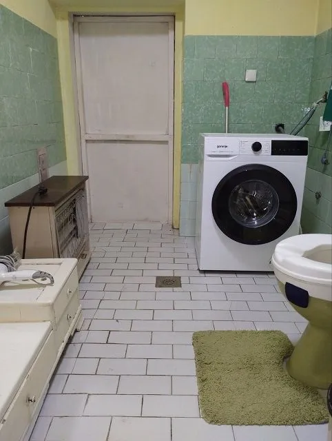Kupatilo sa veš mašinom, WC šoljom i pločicama na zidovima.