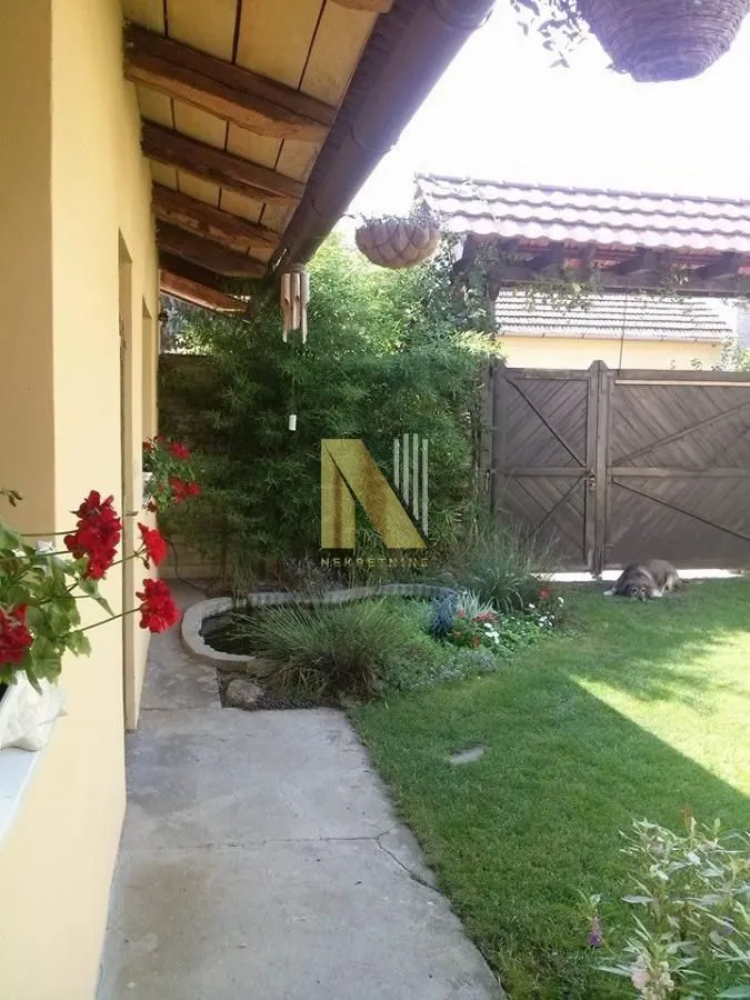Pogled na uređeno dvorište sa travnjakom, baštom i stazom pored kuće.