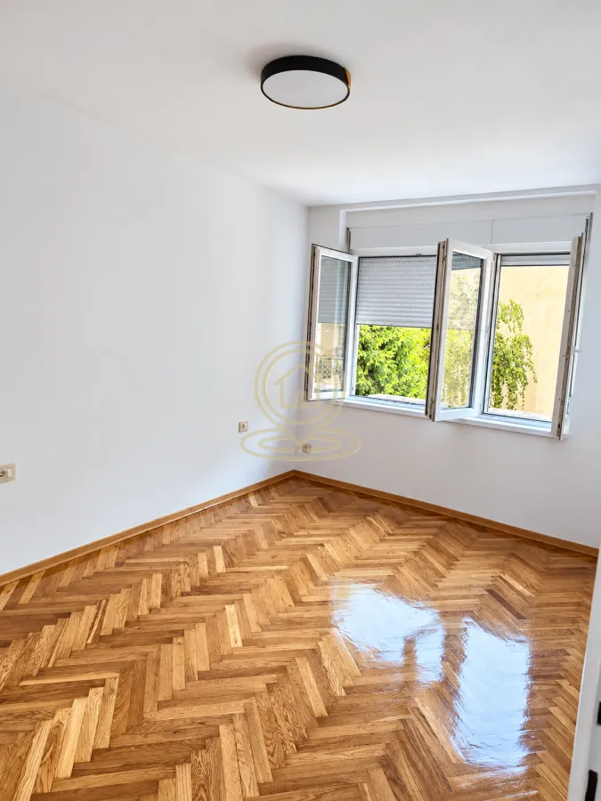 Empty room with white walls and wooden parquet flooring.