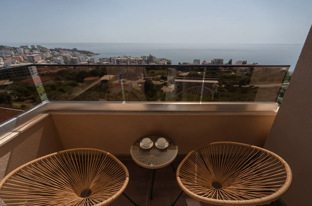 Manji namješteni balkon sa stolom, stolicama i pogledom na more.