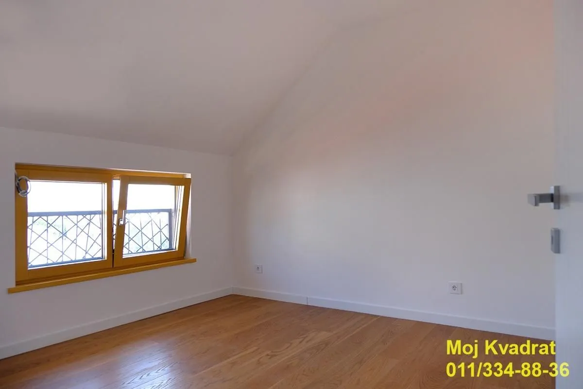 Prazna soba sa kosim plafonom i drvenim podom.