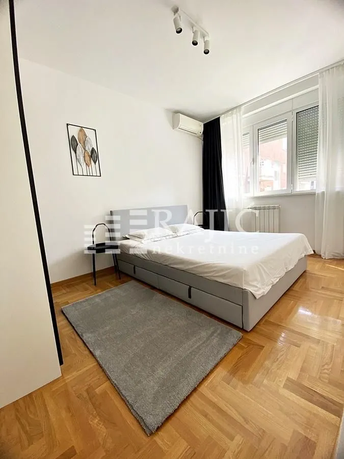 Tidy bedroom with a double bed, parquet flooring, and a window.