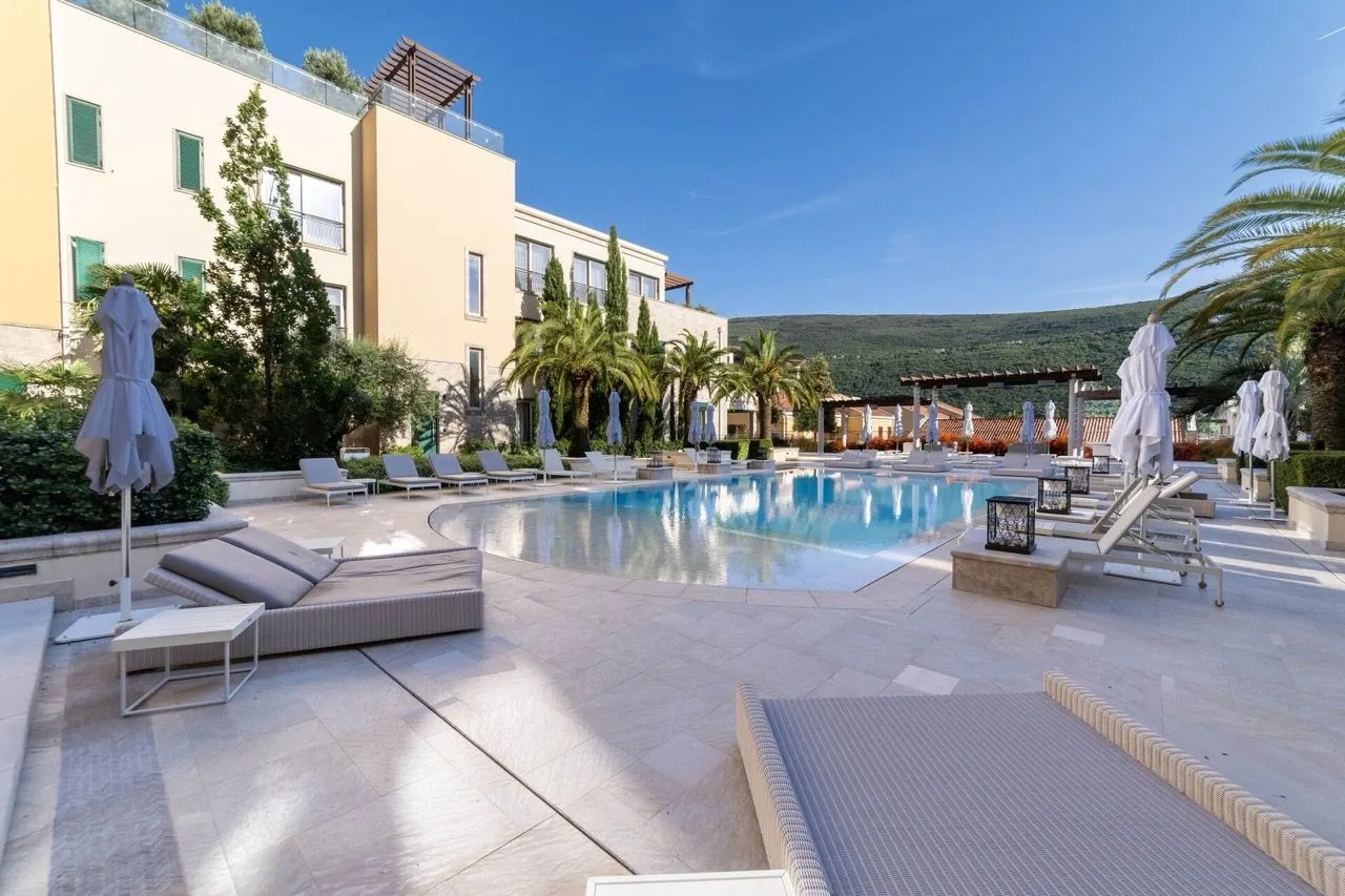 Prostrani vanjski bazen sa ležaljkama i sunkobranima ispred stambenog objekta.
