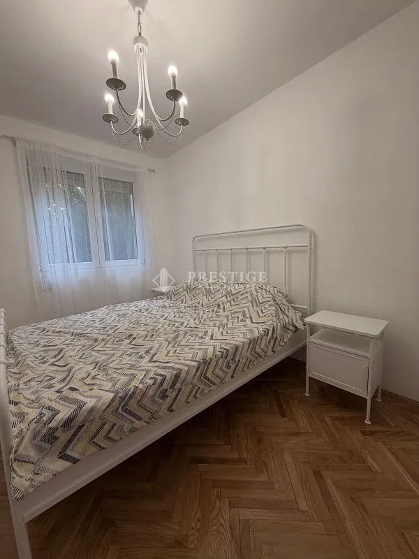 Spavaća soba sa bračnim krevetom, noćnim stočićem i lusterom.
